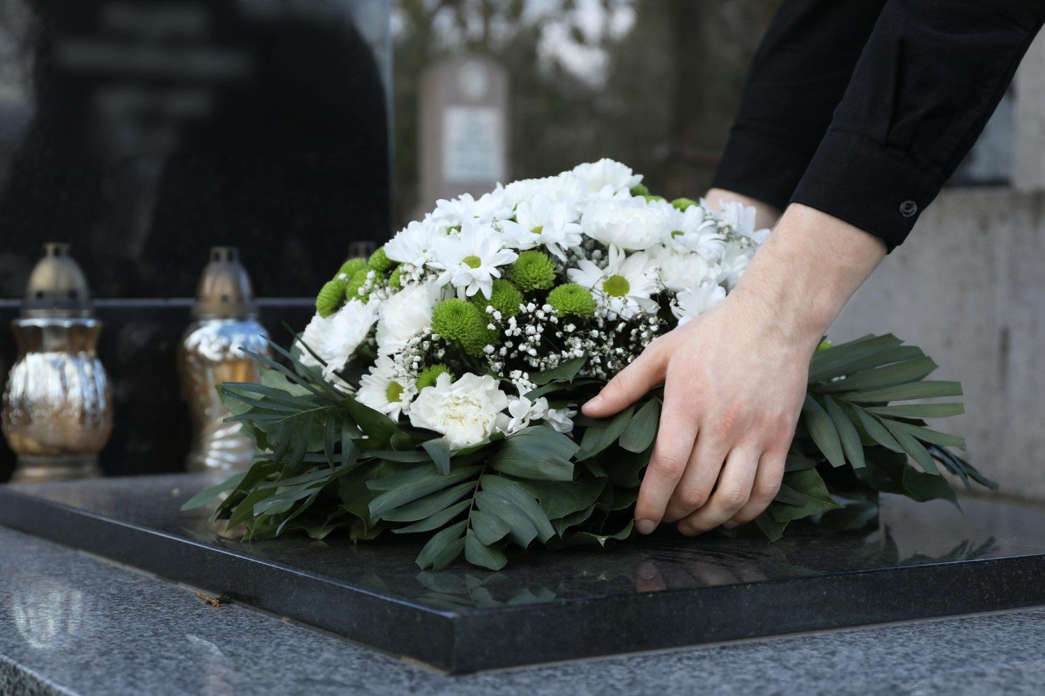 Woman putting funeral wreath of flowers on granite tombstone